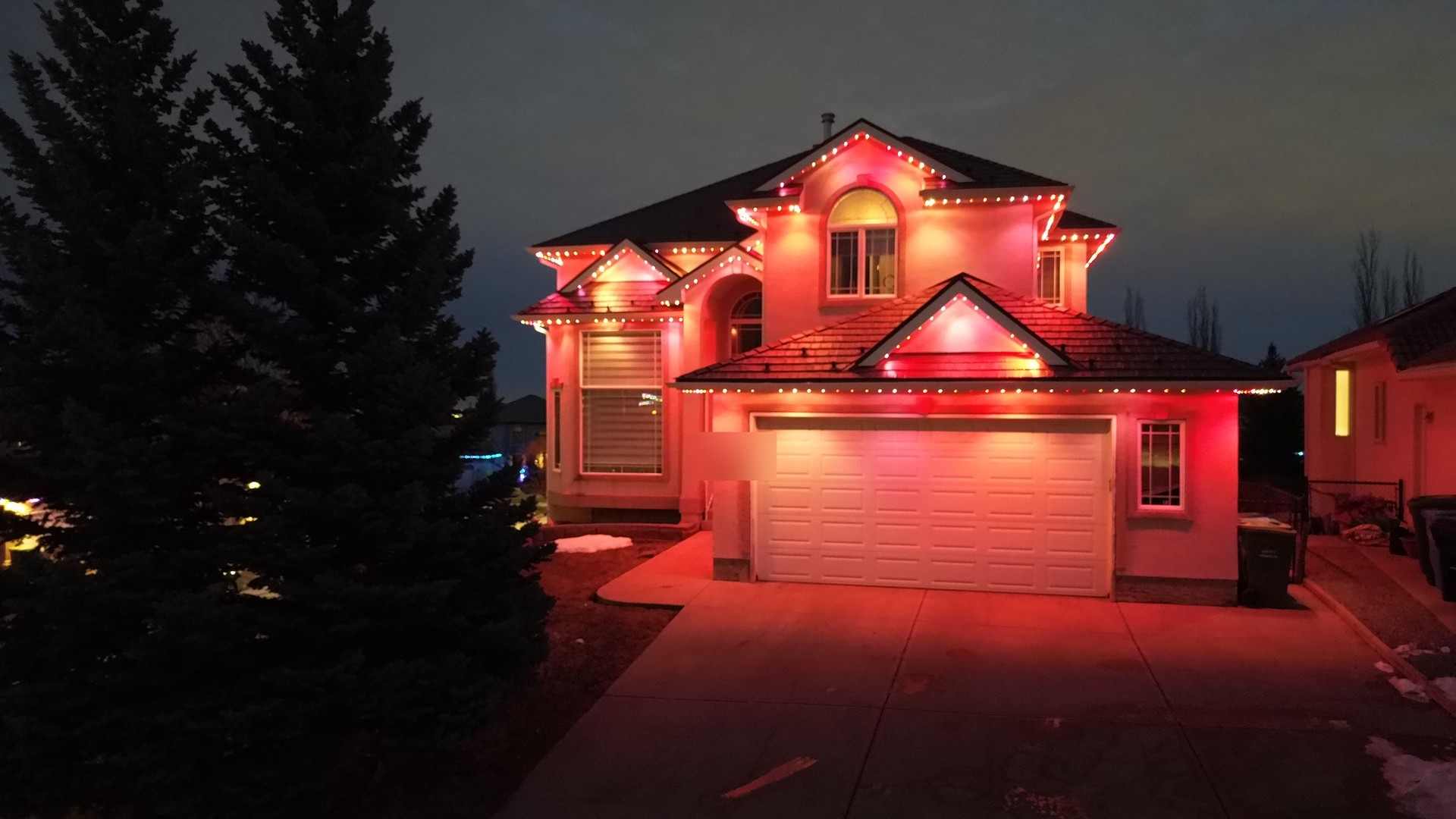 The same home after dark lit entirely in red, the roofline lights reading as a single continuous run.